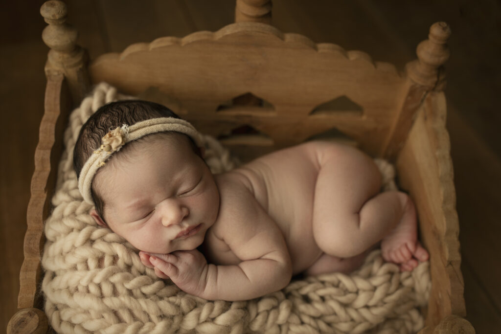 sweet baby girl laying in side pose on a wooden bed.